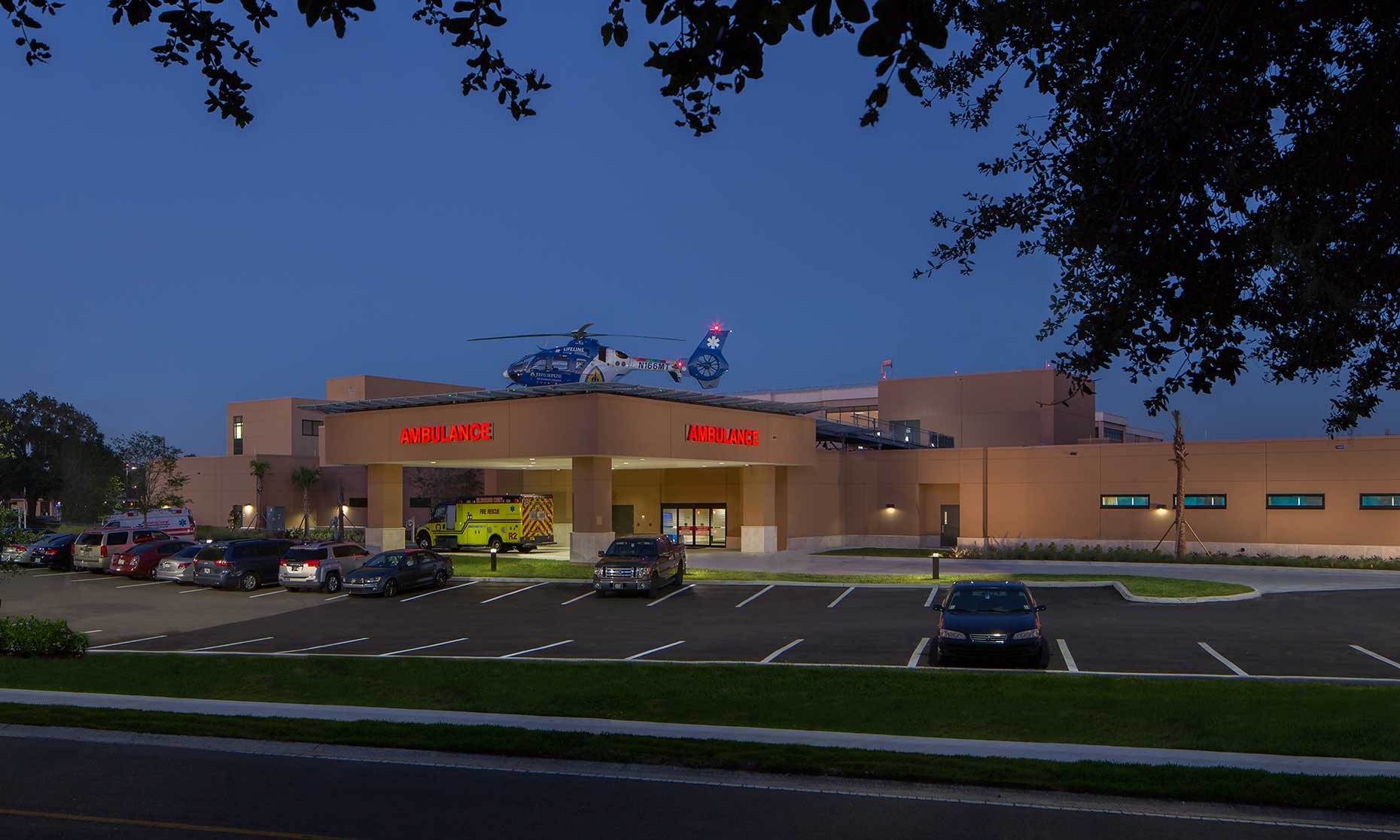 A photo of the ER entrance at twilight with an ambulance and helicopter landed on the roof of Brandon Regional Medical Center