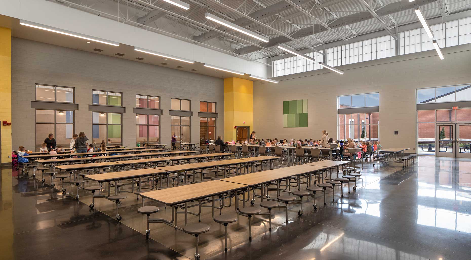 An interior view of students beginning lunch in the multi-purpose room of Crestline Elementary School, with staff assisting in organizing the lunch process