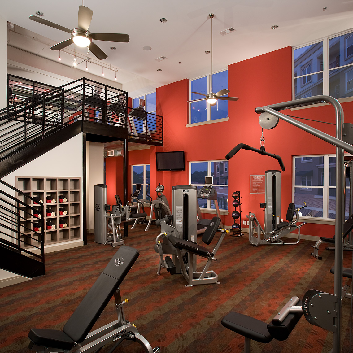 A photo of the two-story fitness center at Goodwynn at Town Brookhaven at twilight, featuring a red wall