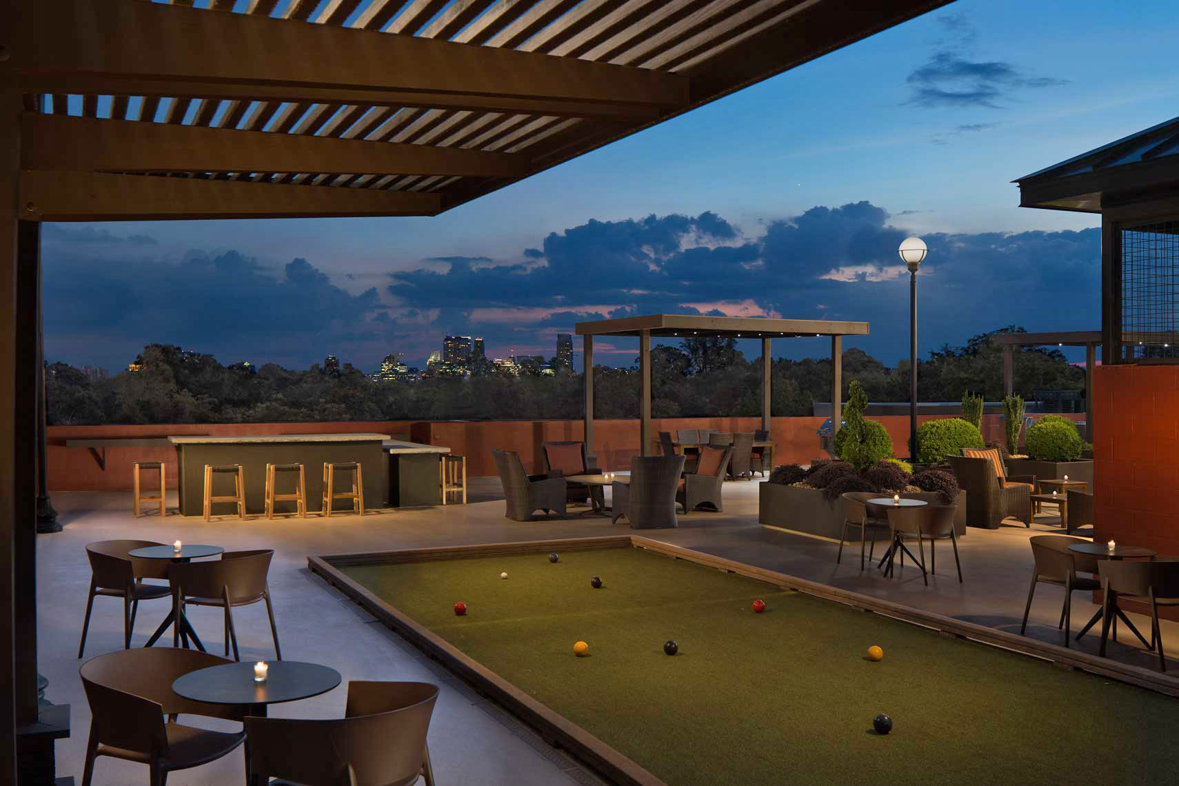 A photo of the rooftop bocce court at Goodwynn at Town Brookhaven at twilight, featuring a view to downtown Atlanta