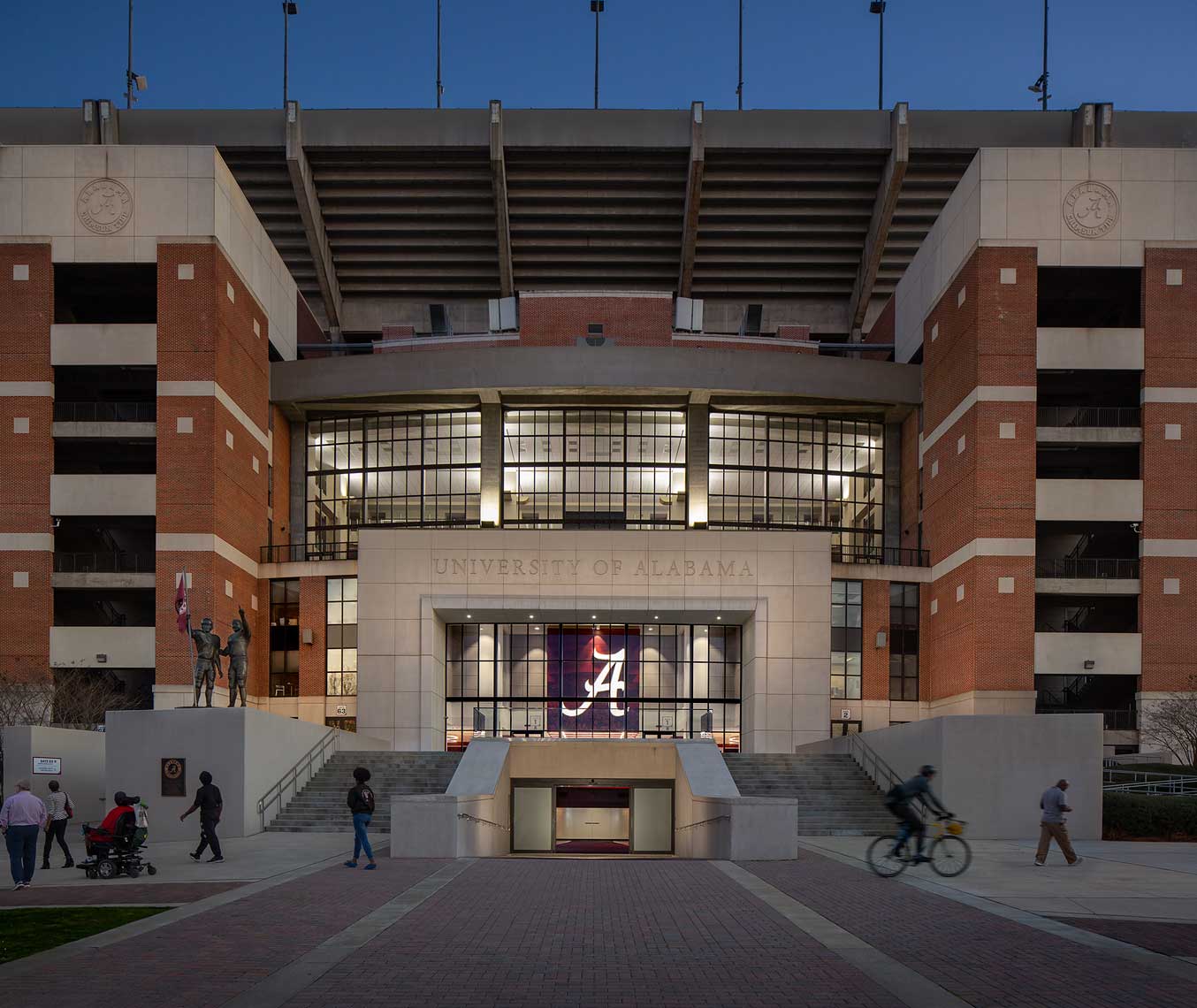 Fans walk by the player entrance to the University of Alabama Bryant-Denny Stadium at twilight