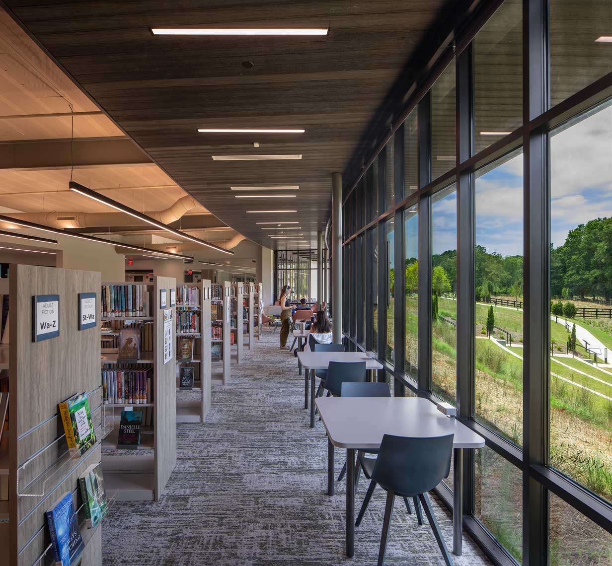 An interior view of the Denmark Branch Library showing the book stacks and the view outside to the natural landscape.