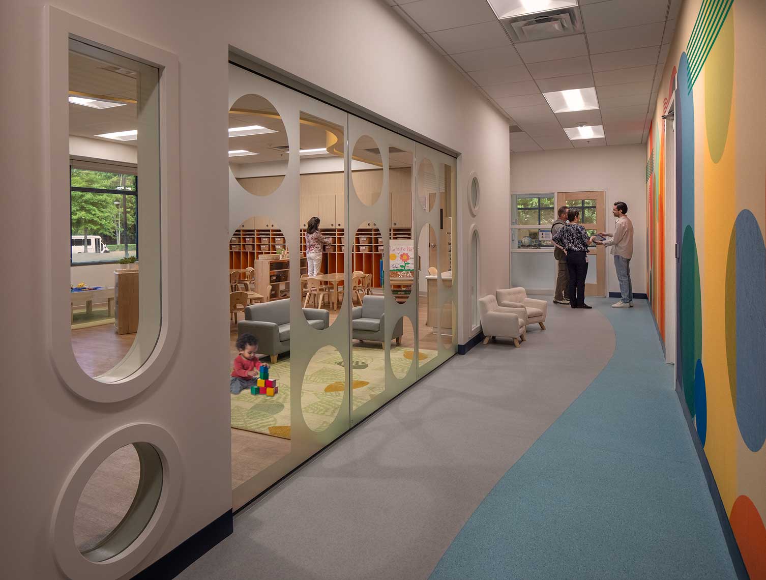 A view down the hallway of the AlleGro Early Learning Center, showing parents and a teacher conferring, and a view into a charming classroom