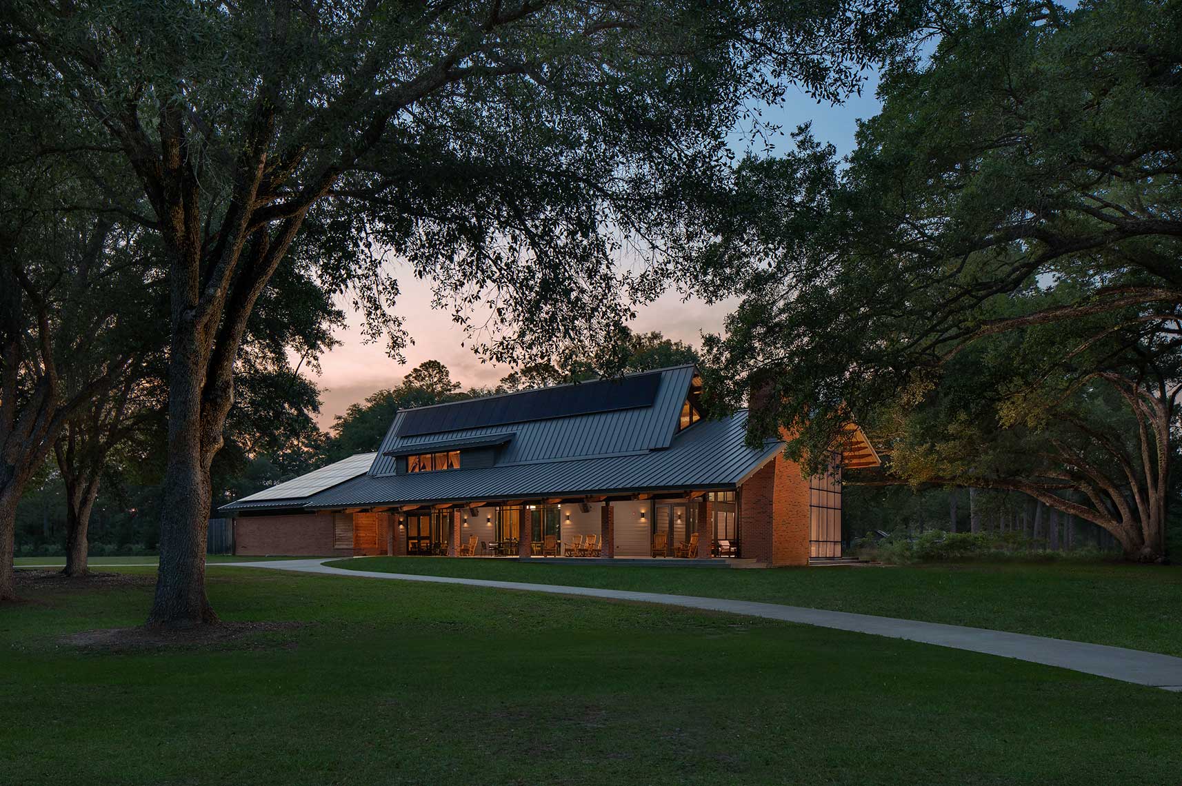 A twilight view of the exterior of The Jones Center at Ichauway, showing the rustic design and surrounding live oak trees