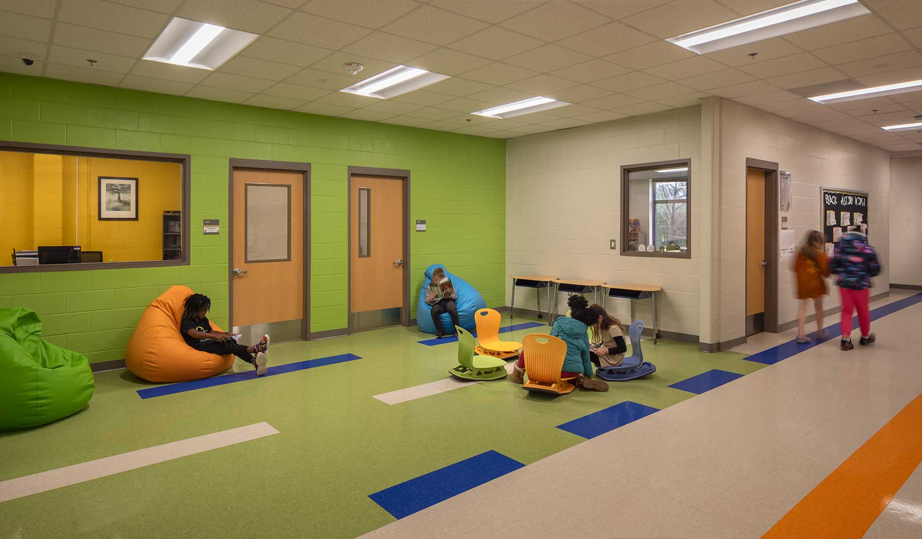 An interior view of the colorful collaboration area within Toomer Elementary School, showing students reading amidst the furniture