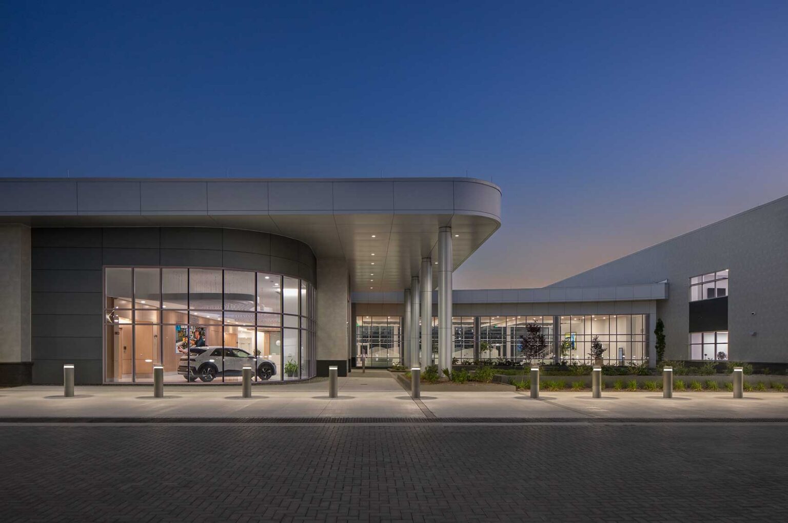 An eye level view at twilight of the Quick Start - Hyundai Mobility Training Center of Georgia by SSOE Group, showing a Hyundai car parked inside the lobby