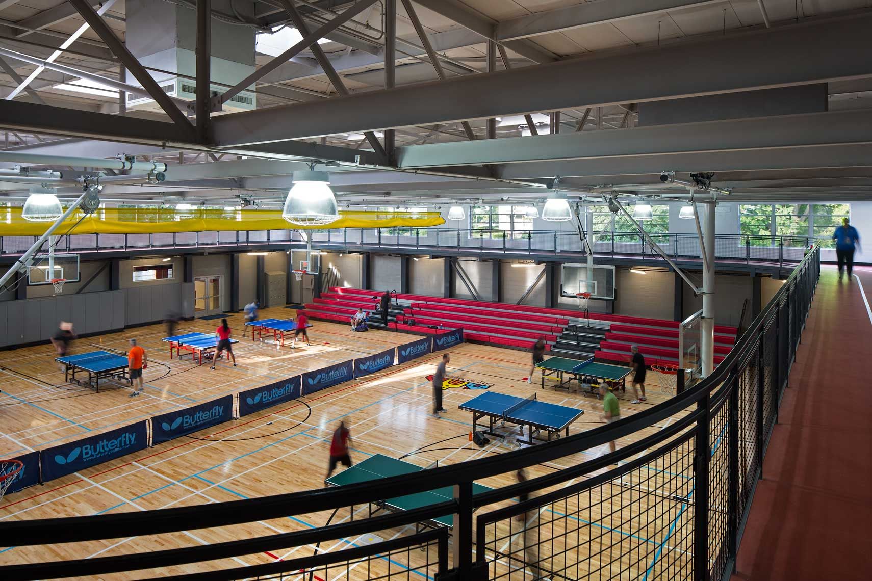 An interior view of the gymnasium at the Decatur Recreation Center featuring many people playing ping pong and walking the track.